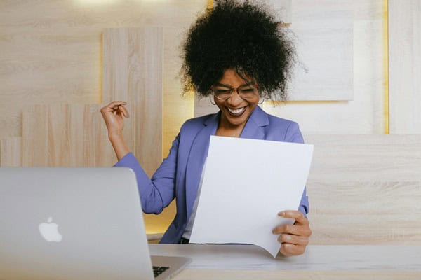 What is An SEO Audit? Woman wearing a purple shirt with a white sheet of paper in front of a silver Apple laptop.