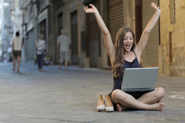 Why do An SEO Audit? Girl sitting cross-legged in front of a silver laptop with arms raised in the air.